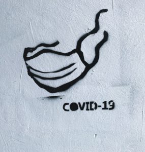 stêncil de máscara pintado em parede brancaao lado da palavra covid-19