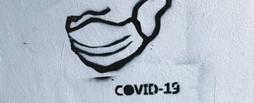 stêncil de máscara pintado em parede brancaao lado da palavra covid-19