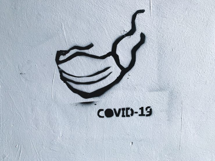 stêncil de máscara pintado em parede brancaao lado da palavra covid-19