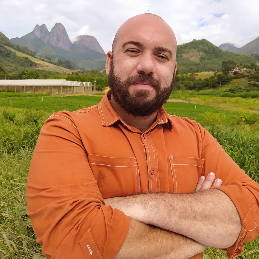 Ádison Ramos, em imagem que o mostra do tronco para cima, em fundo de pasto. Ele é um homem branco, careca de barba castanha cheia.