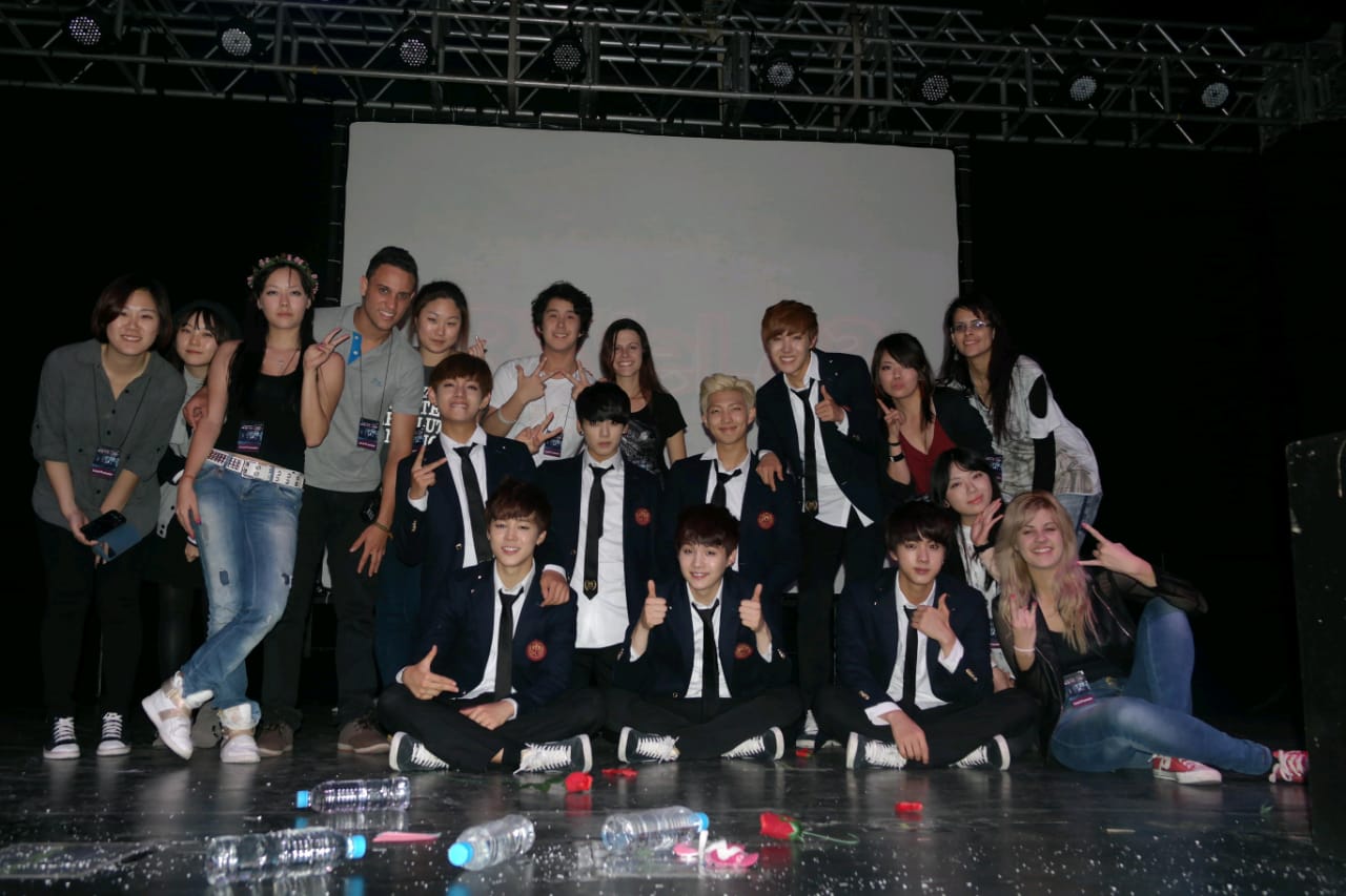 Sete membros do grupo BTS vestidos com terno e dez fãs com roupas casuais posando para uma foto descontraída.