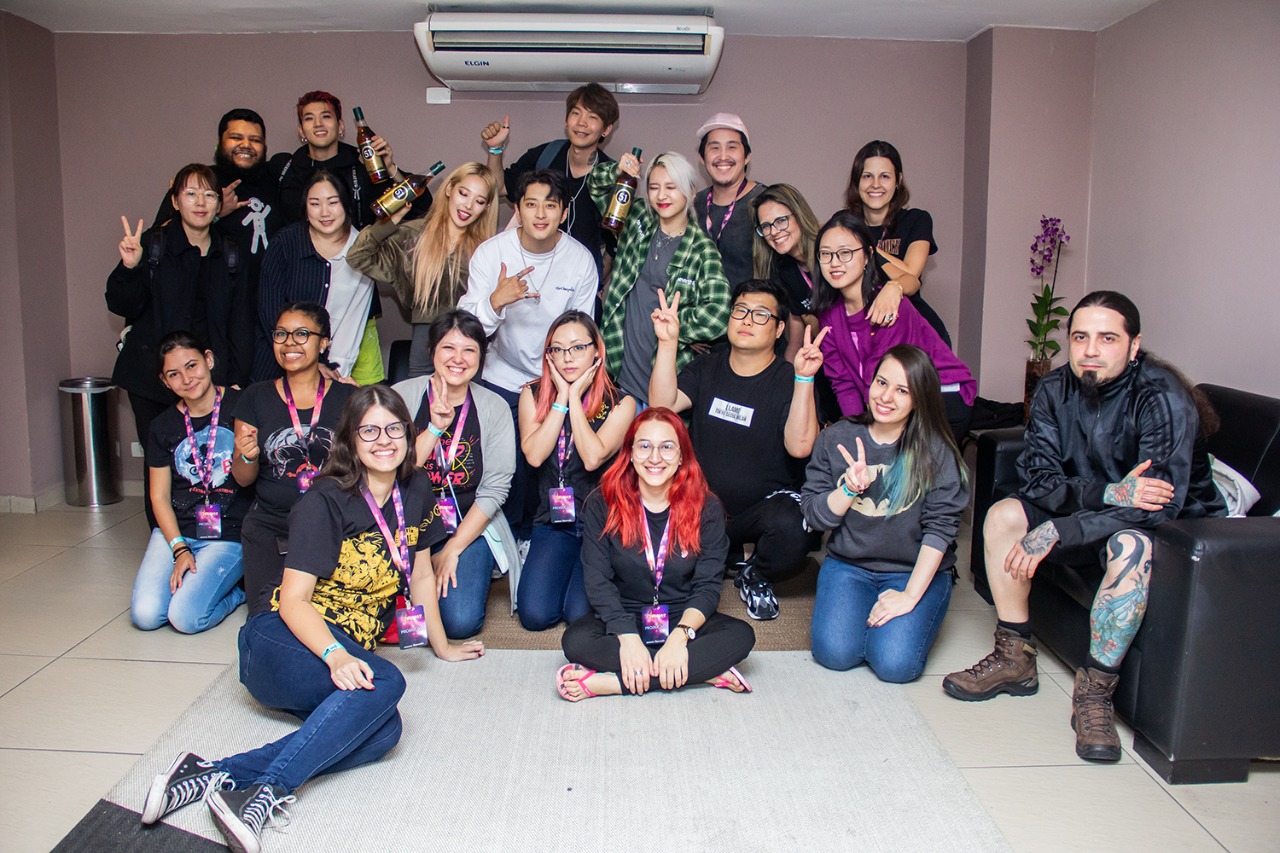 Quatro membros do grupo KARD e dezessete fãs com roupas casuais posando para foto descontraída.