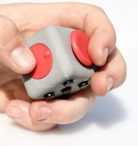 A mão de uma pessoa branca segura um fidget toy em formato de cubo