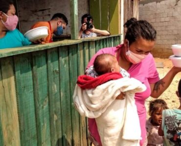 Mãe retirando marmitas para alimentar seus filhos. Entre eles, um bebê.