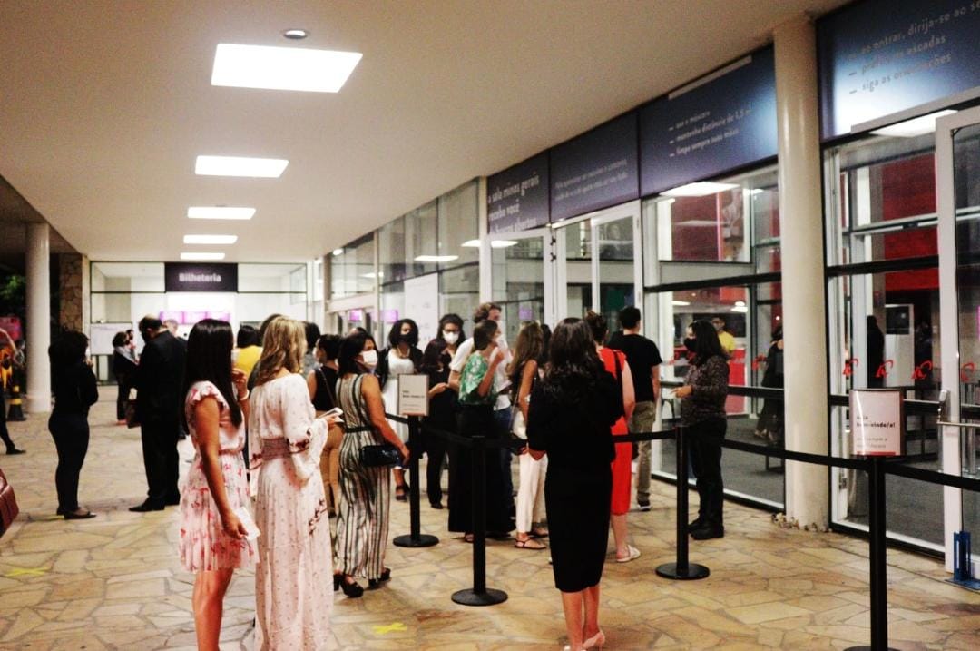 Pessoas usando máscaras de proteção facial aguardam em fila na entrada da Orquestra Filarmônica, a espera para adentrar o local do próximo espetáculo.