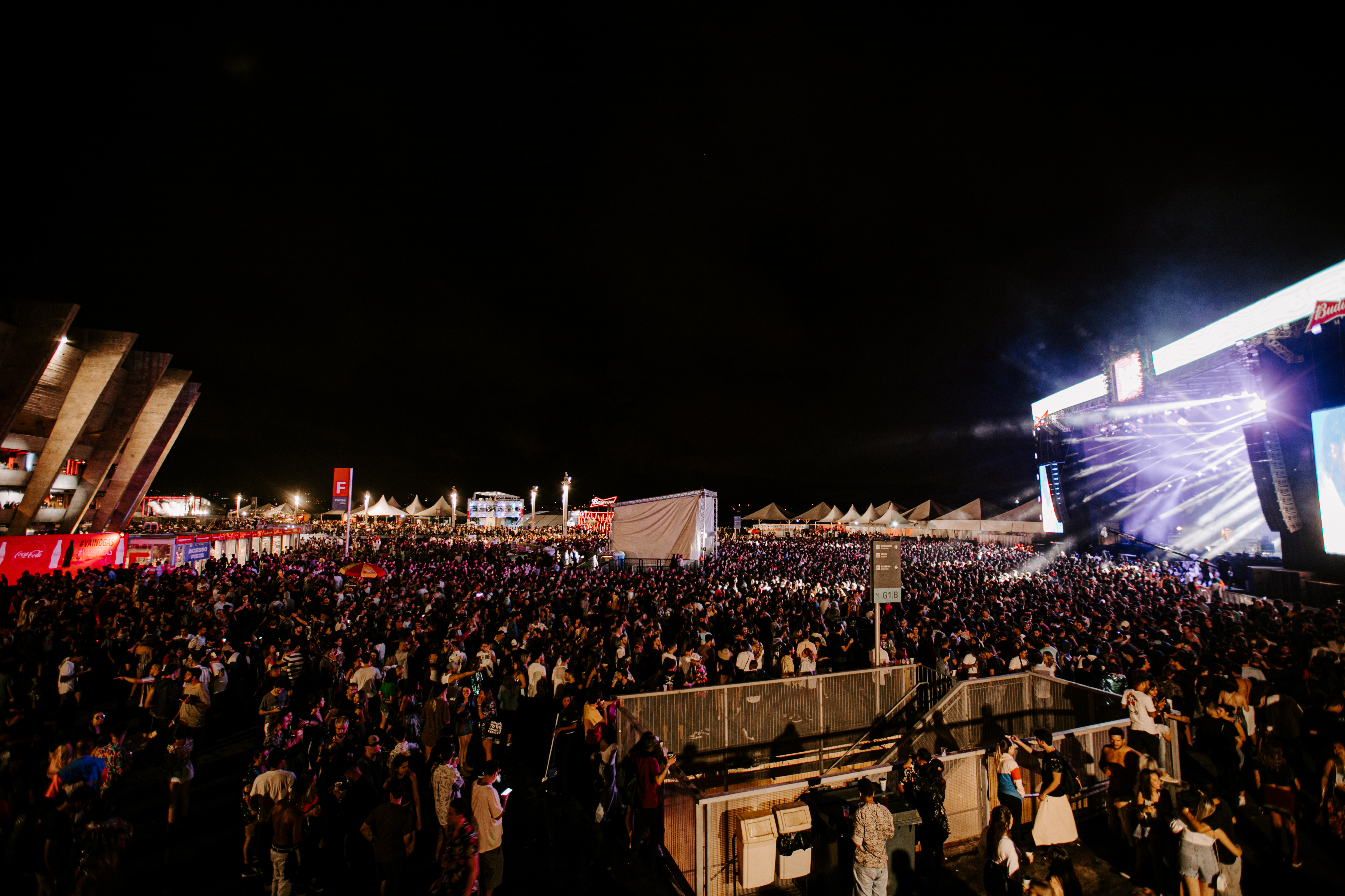 Foto noturna mostra uma vista panorâmica do Festival Planeta Brasil. À esquerda é possível ver o Mineirão, a esplanada está com um grande público que assiste ao show em um palco à direita da imagem.