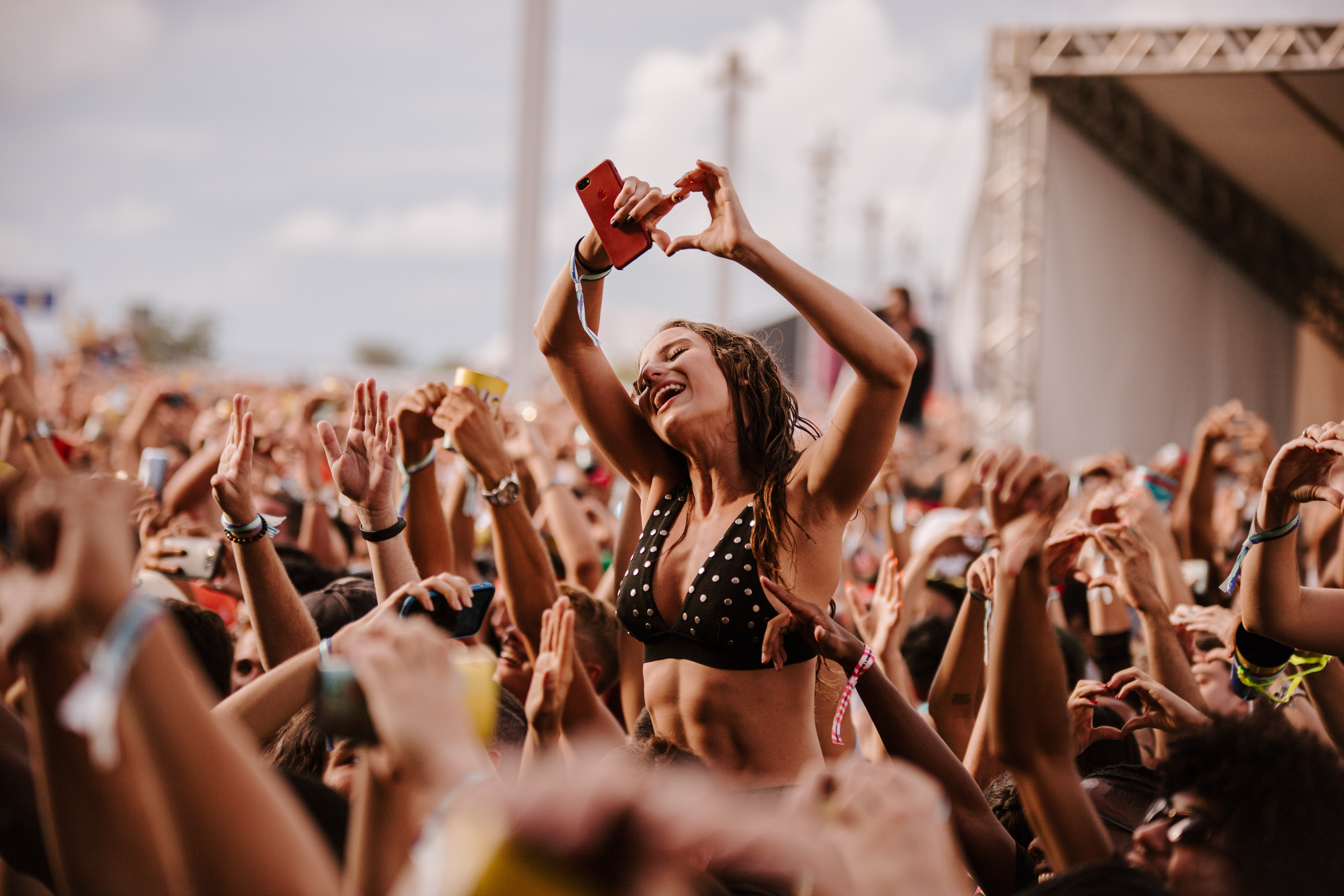 Jovem mulher se diverte em meio a multidão no Festival Planeta Brasil. Ela se destaca em meio a multidão fazendo um coração com as mãos enquanto assiste ao show.