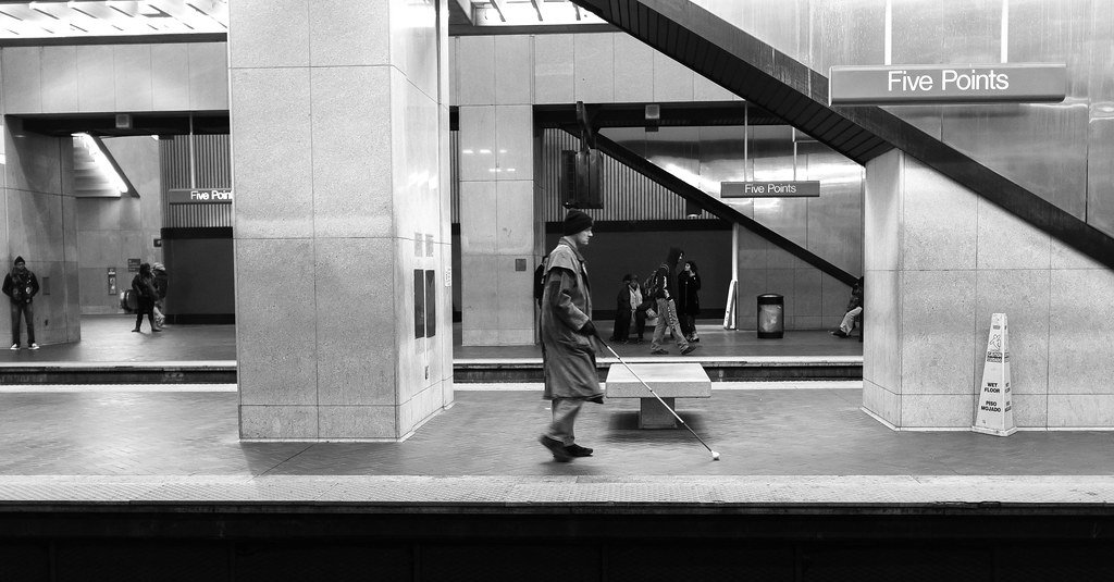Homem anda em plataforma de metrô vazia usando uma varinha para pessoa com deficiência visual.
