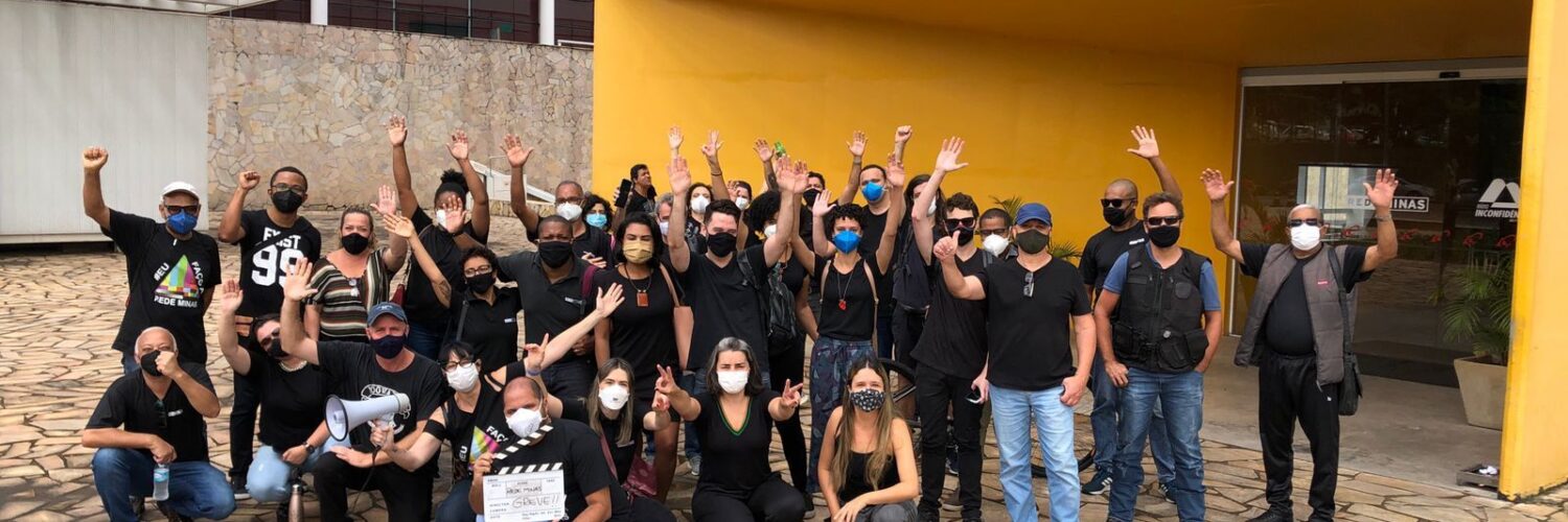 Grupo de pessoas vestidas de preto, em frente a um prédio de entrada amarela e janelas de vidro