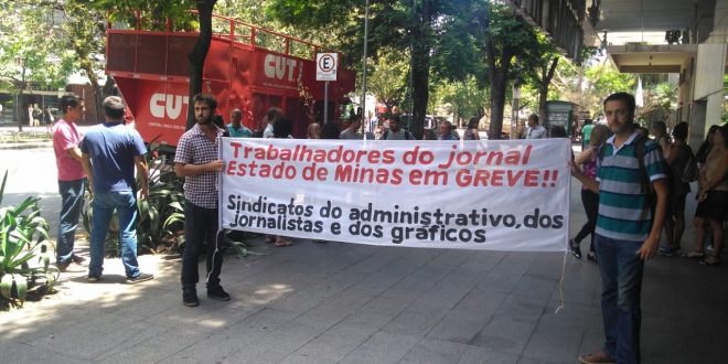 Dois homens seguram uma faixa com a mensagem: "Trabalhadores do jornal Estado de Minas em Greve!! Sindicato dos administrativos, dos jornalistas e dos gráficos".