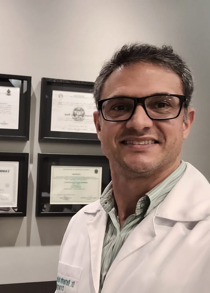 O médico Bernardo Nalon em frente a certificados na parede, cabelos grisalhos, usando óculos de grau e jaleco