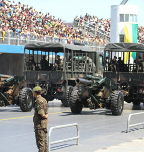 foto de desfile militar mostrando soldado em primeiro plano e carros militares ao fundo