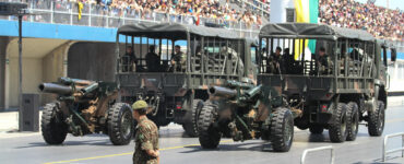 foto de desfile militar mostrando soldado em primeiro plano e carros militares ao fundo