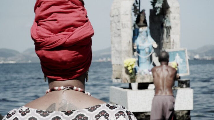 imagem de mulher negra com turbante vermelho de costas olhando para imagem de yemanja