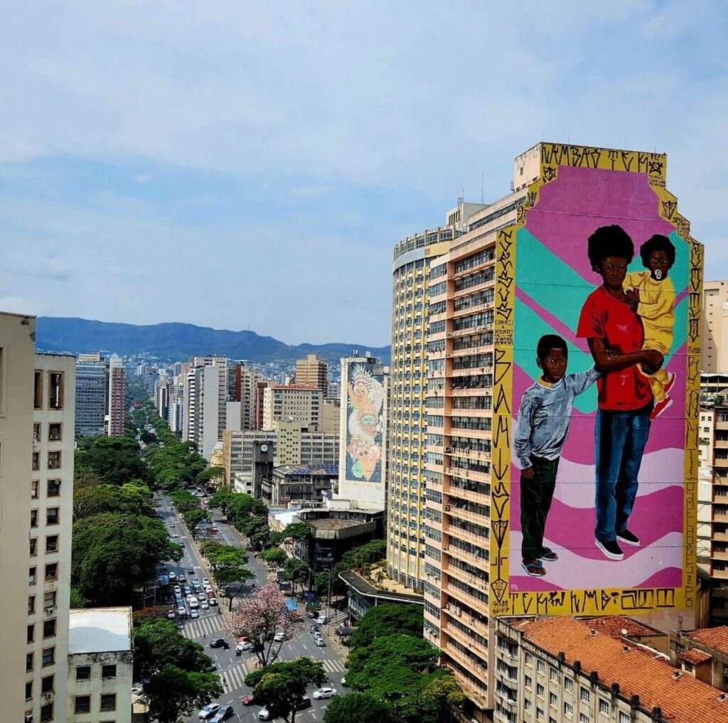 Fotografia colorida com visão aérea do centro de Belo Horizonte. À direita, em primeiro plano, painel do projeto CURA em empena de prédio