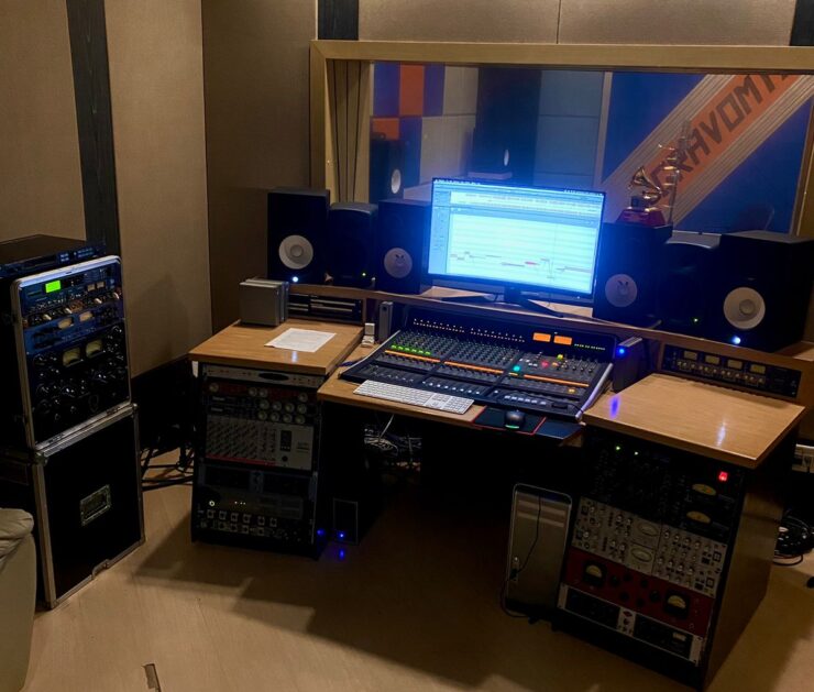 Foto do estúdio principal do Estúdio Gravomix. Em primeiro plano, Mesa de som, computador com a tela ligada. Em segundo plano, estúdio de captação de áudio.