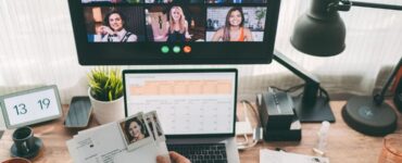 Descrição de imagem: ambiente de escritório, com computador aberto em uma tabela, uma tela a frente com pessoas na videochamada.