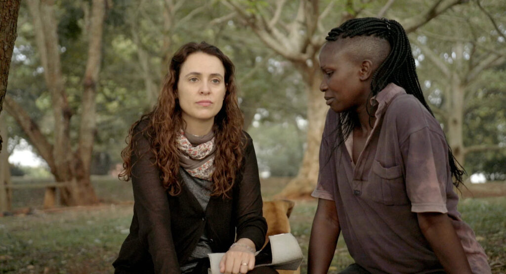 Fotografia de trecho do filme, em que Joana, branca, de cabelos castanhos e ondulados e Kevin, negra, de cabelos trançados estão conversando em um parque.