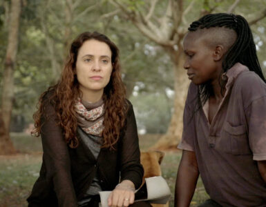 Fotografia de trecho do filme, em que Joana, branca, de cabelos castanhos e ondulados e Kevin, negra, de cabelos trançados estão conversando em um parque.