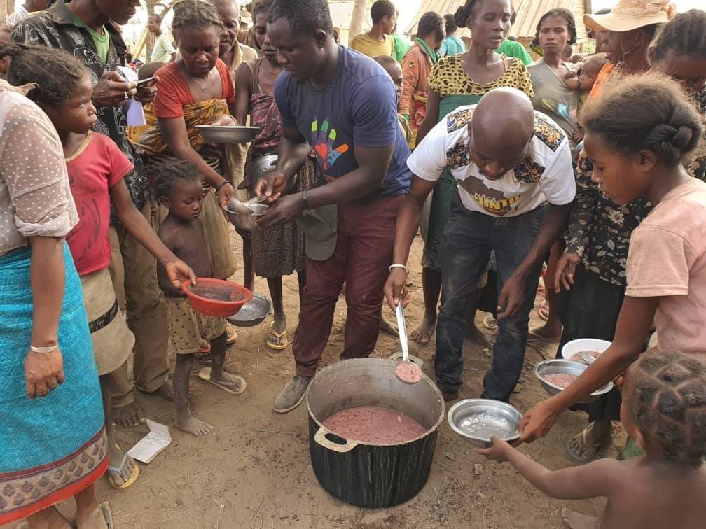 Descrição de imagem: Felly Zihal usando uma camiseta azul e calça vermelha e voluntários da ONG Fraternidade Sem Fronteiras distribuindo alimento para famílias necessitadas em tribo no Madagascar.