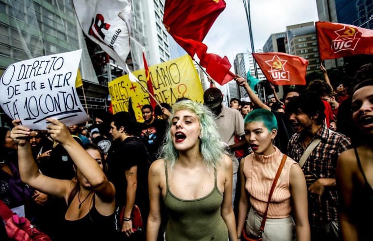  Foto de autoria de Gabriela Biló durante manifestação do Movimento Passe Livre e mostra diversas mulheres protestando, além de bandeiras com coloração forte (vermelhas e amarelas)
