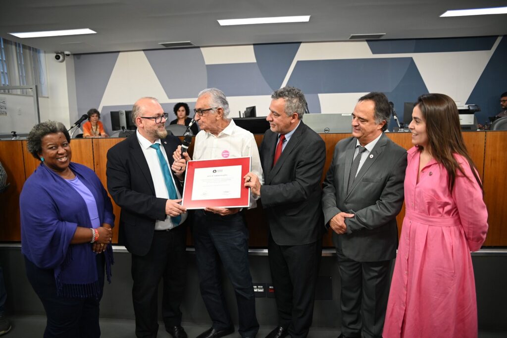 Da esquerda para a direita: os deputados estaduais Macaé Evaristo (PT), cabelos grisalhos, com roupa na cor roxa; o professor Cleiton (PV), careca, barba clara, óculos de grau pretos, terno preto e gravata azul, acompanhados de Ricardo Parreiras, com camisa social branca, calça preta, segurando uma placa; e dos deputados estaduais doutor Jean Freire (PT), de terno preto e gravata vermelha; Mauro Tramonte (Republicanos), de terno e gravata cinza; e Lohanna Lima (PV), com cabelos castanhos e usando vestido rosa.
