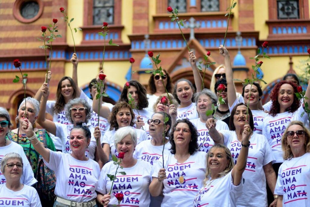 Mulheres brancas do movimento "Quem Ama Não Mata" segurando rosas vermelhas em frente a Igreja São José.