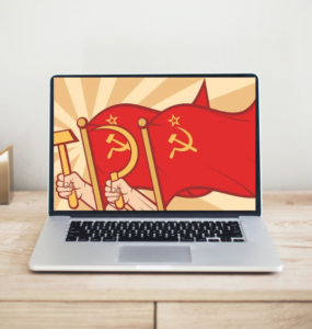 Na imagem, um computador no centro com bandeiras comunistas na tela. No lado esquerdo, um artigo de decoração e no lado direito um vaso de plantas.