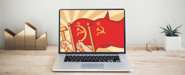 Na imagem, um computador no centro com bandeiras comunistas na tela. No lado esquerdo, um artigo de decoração e no lado direito um vaso de plantas.