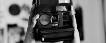 Foto em preto em branco de um adolescente utilizando câmera analógica de impressão instantânea.