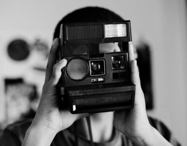 Foto em preto em branco de um adolescente utilizando câmera analógica de impressão instantânea.