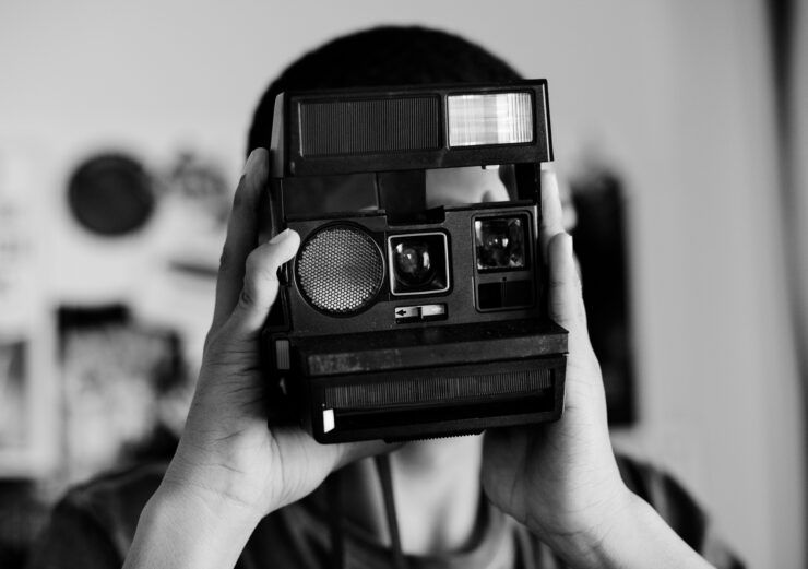 Foto em preto em branco de um adolescente utilizando câmera analógica de impressão instantânea.