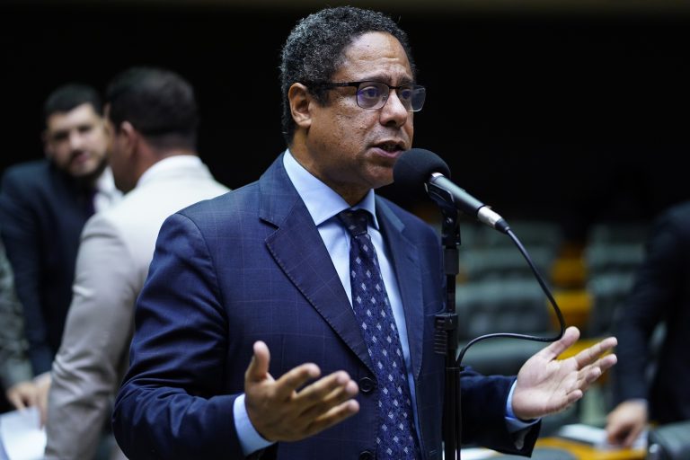 Alt: Orlando Silva (PCdoB-SP), homem negro de terno, discursando no plenário da Câmara dos Deputados em frente a um microfone.