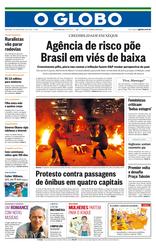 Capa do jornal O Globo, dia 7 de junho de 2013. A manchete do jornal é “Agência de risco pões Brasil em viés de baixa”. A foto que compõe a capa foi tirada em espaço aberto, durante a noite, em um protesto com pessoas adultas colocando fogo em cones na avenida 9 de julho em São Paulo. Abaixo tem outro destaque “Protesto contra passagens de ônibus em quatro capitais”.