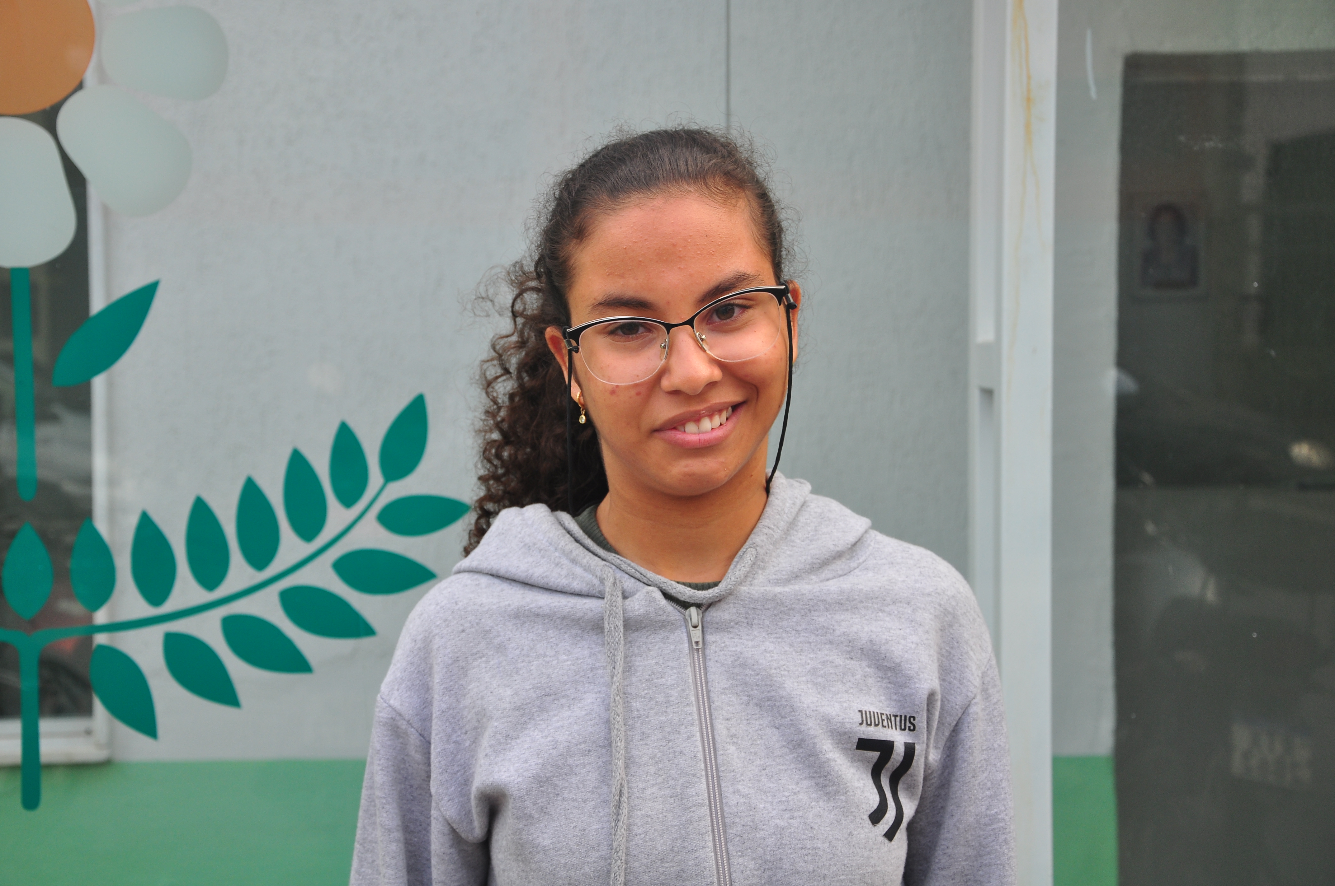 Maria Vitória, 13 anos, sorri em frente à fachada da APAE, clínica onde tem acompanhamento médico e social. 
