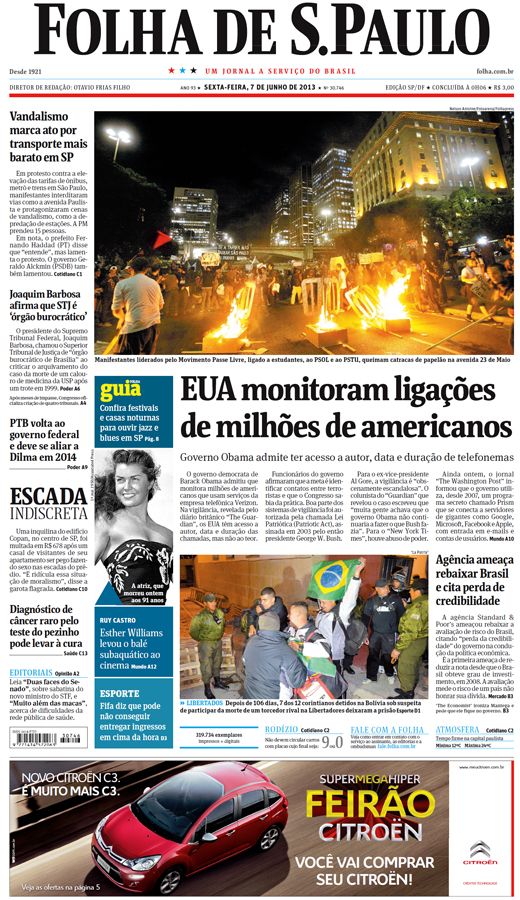 Capa do jornal Folha de São Paulo, dia 7 de julho de 2013. A foto destacada foi feita em um ambiente aberto, durante a noite, em um lugar cercado por prédios e registra manifestantes ateando fogo em alguns objetos no chão. O título da capa do jornal é “Vandalismo marca ato por transporte mais barato em SP.”