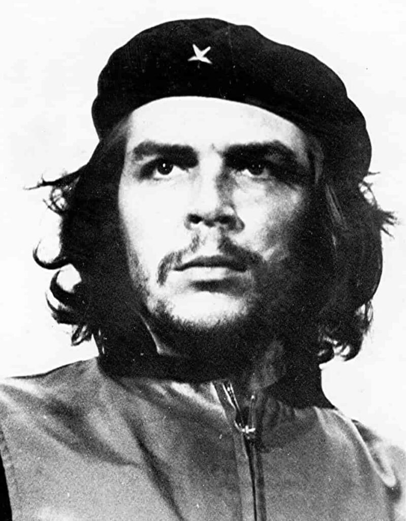 Fotografia em preto e branco do revolucionário Che Guevara. Na imagem ele usa uma boina cobrindo seus cabelos longos enquanto olha para o horizonte