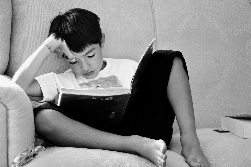 foto em preto e branco de menino sentado no sofá lendo um livro 
