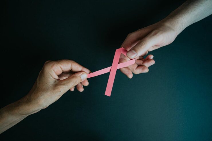 Imagem de laço rosa, símbolo da campanha outubro rosa, sendo repassado de uma mão para outra.
