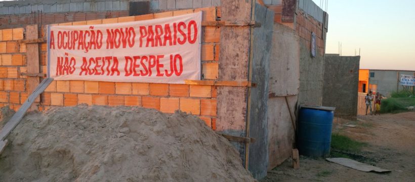 Casa de tijolos na ocupação Novo Paraíso, na parede externa da casa há um cartaz onde se lê: "A ocupação Novo Paraíso não aceita despejo"