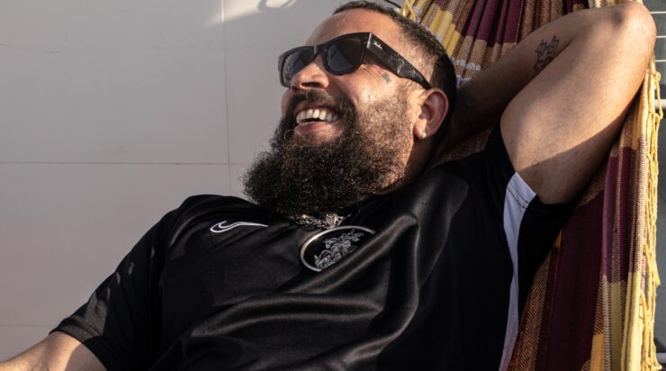 FBC, homem branco, com barba grande, deitado na rede com o braço esquerdo atrás da cabeça e sorrindo.