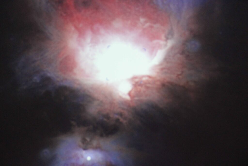 Imagem de uma nuvem interestelar de poeira, hidrogênio, hélio e outros gases. Cores predominantes são vermelho, preto e branco.