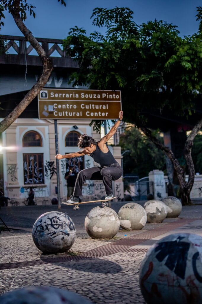 Lorena Fernanda, atleta de skate, exercendo manobra sobre pedras redondas embaixo do Viaduto Santa Tereza. 