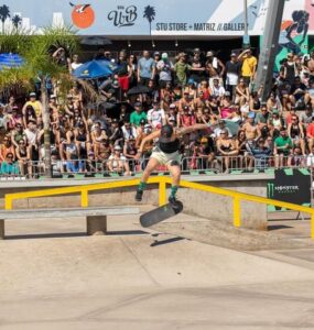 Atleta de skate de boné preto exercendo manobra sobre um corrimão amarelo