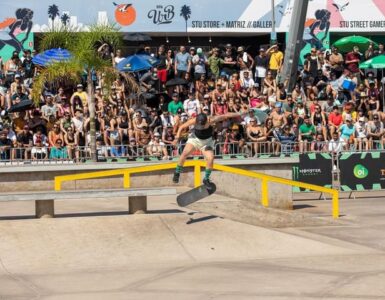 Atleta de skate de boné preto exercendo manobra sobre um corrimão amarelo