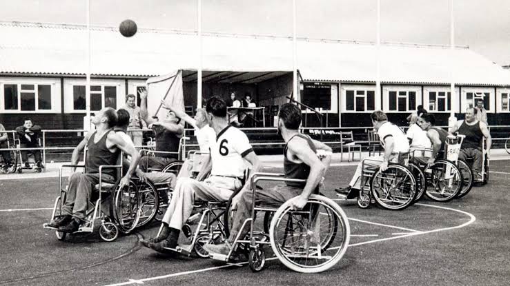 Atletas em cadeira de rodas jogam basquete. Foto em preto e branco. 