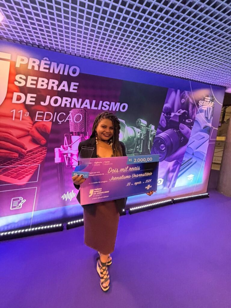 Jovem negra segurando cheque premiado em dois mil reais no evento do Sebrae