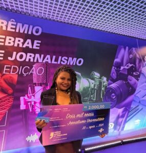 Jovem negra segurando cheque premiado em dois mil reais no evento do Sebrae