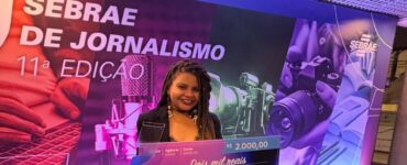 Jovem negra segurando cheque premiado em dois mil reais no evento do Sebrae