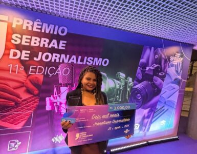 Jovem negra segurando cheque premiado em dois mil reais no evento do Sebrae